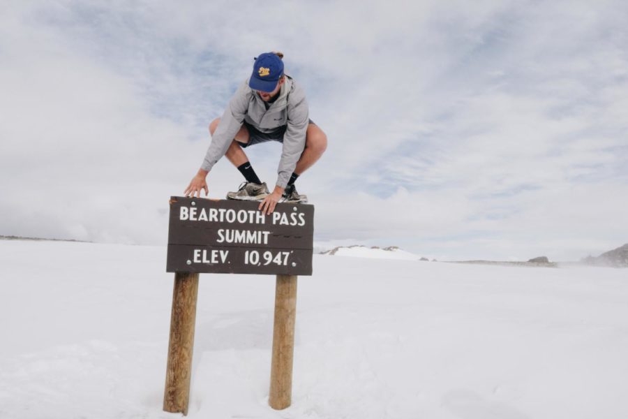 Levko crouches on top of a Beartooth Pass Summit sign surrounded by snow this summer. (Photo courtesy of Levko Karmazyn)