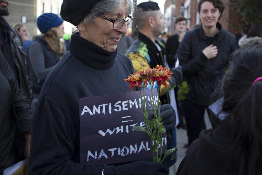  Emily DeFerrari of Point Breeze handed out flowers to mourners, holding a sign reading antisemitism = white nationalism” at Tuesday’s march in Squirrel Hill. 