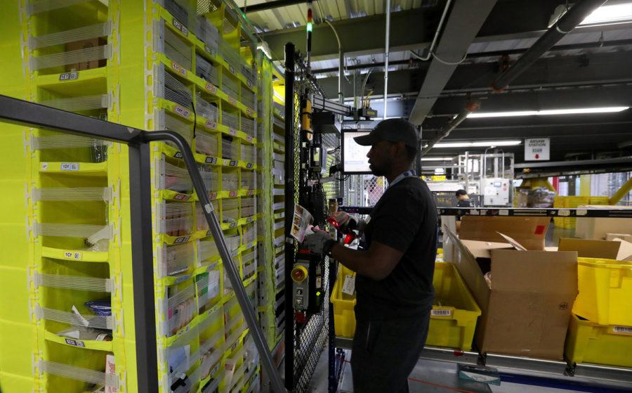 An Amazon worker scans items with a handheld device before putting them in storage pods maneuvered by robots. Amazon announced its plan to roll out a $15-an-hour minimum wage for all of its U.S. employees.