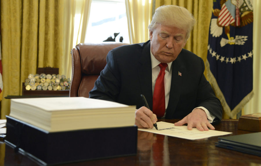 President Donald J. Trump signs the $1.5 trillion tax cut bill, stacked on his desk, in the Oval Office on December 22, 2017 in Washington, D.C. The New York Times recently released an investigative report that confirmed Trump committed approximately $413 million of tax evasion over several years.