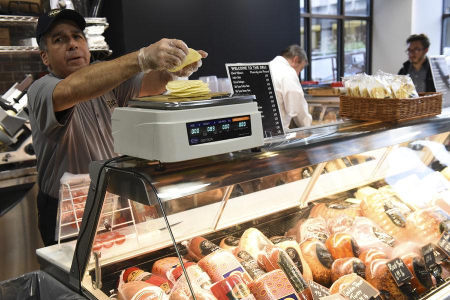 An employee at Forbes St. Market weighs cheese on the deli’s scale.