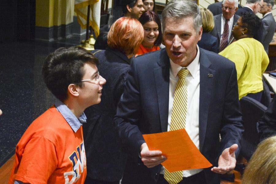 Chancellor Patrick Gallagher talks to members of the Fossil Free Pitt Coalition, wearing orange t-shirts over formal dress, at Pitt's 2017 winter Board of Trustees Meeting in the William Pitt Union. 