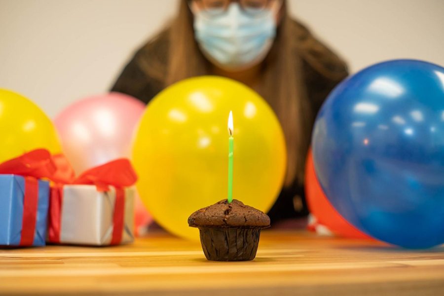 A woman blows out a birthday candle while wearing a mask.