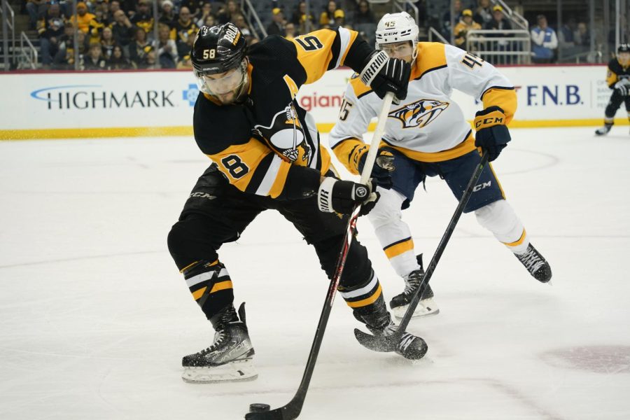 Kris Letang (58) of the Pittsburgh Penguins brings the puck up ice as Alexandre Carrier (45) of the Nashville Predators defends during Sunday’s game in Pittsburgh.