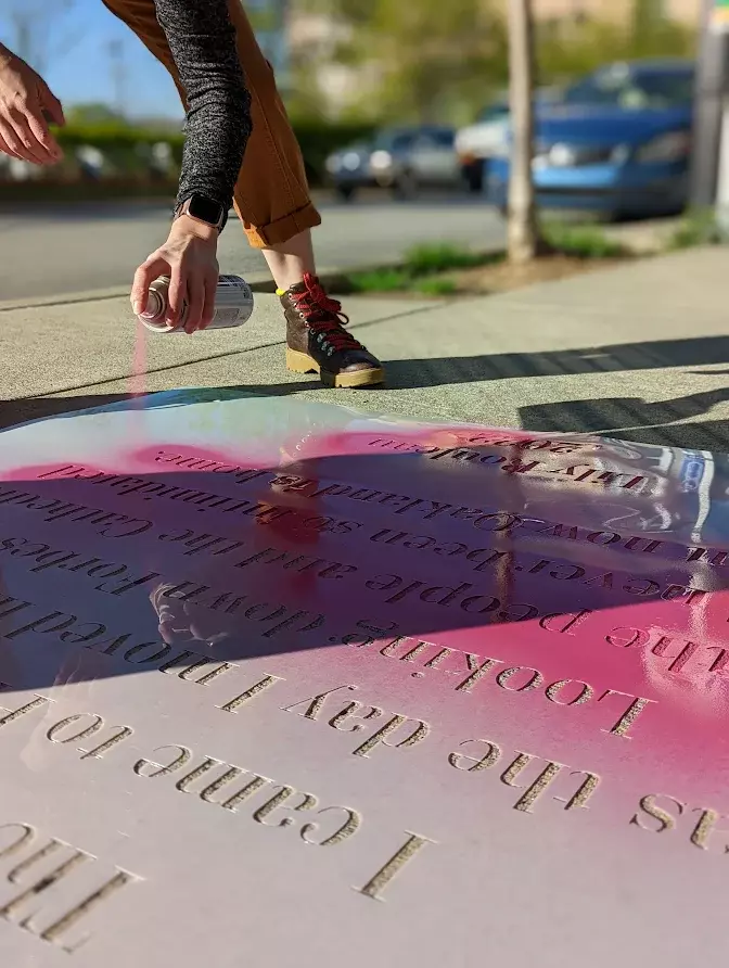 A sidewalk poem being made with pink spray paint. 
