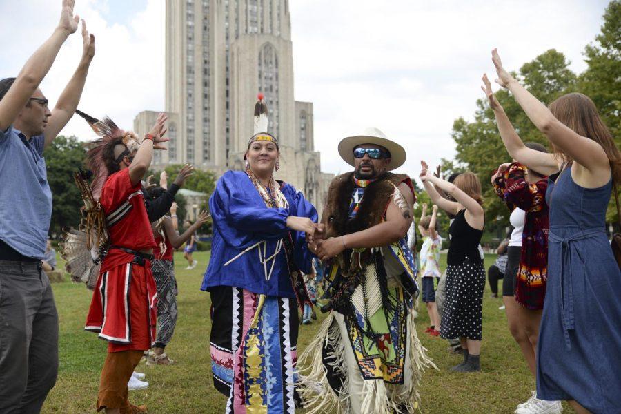 Two COTRAIC dancers hold hands between a group of dancers and community members engaged in a social dance at Wednesday’s mini pow wow in Schenley Plaza. 
