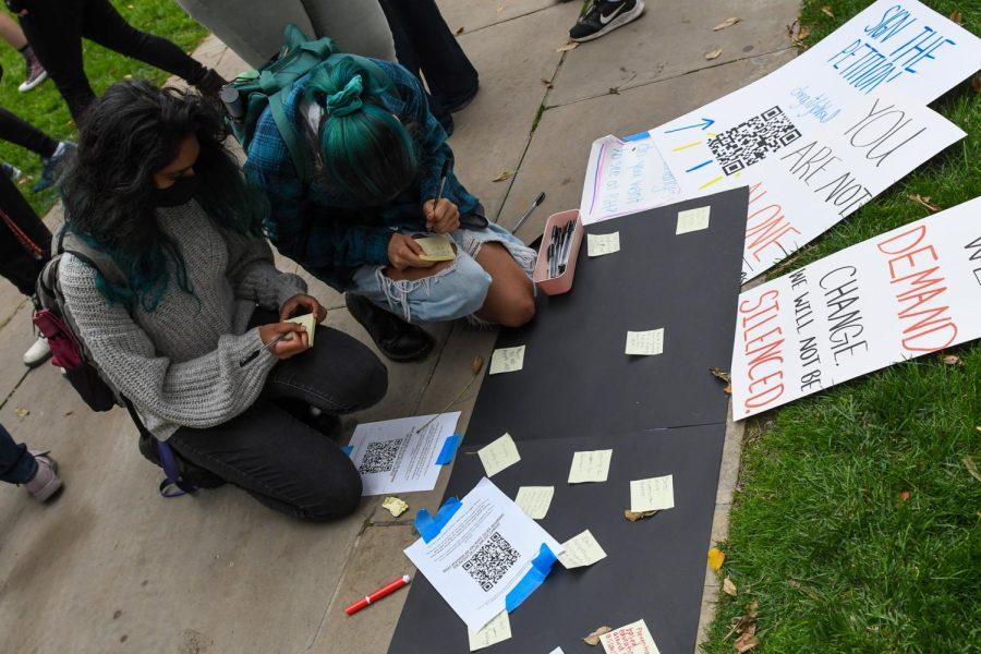 Students write notes of support during a protest against sexual violence outside the Cathedral of Learning Friday afternoon. 