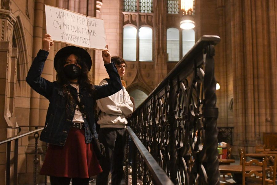A student raises a sign during a protest against sexual violence in the Cathedral of Learning Friday afternoon.