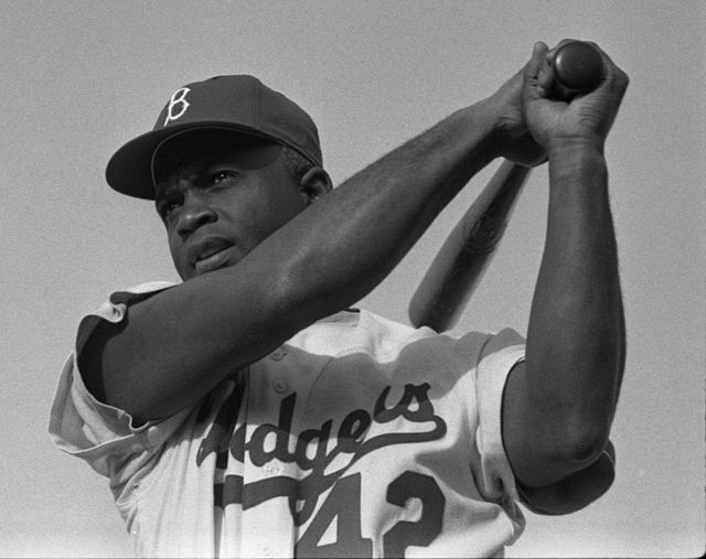 Jackie Robinson swings a bat in a Dodgers uniform in 1954.