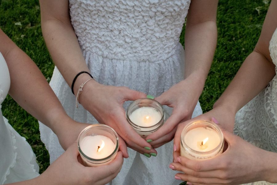 Pitt students pose for a photo wearing white dresses and holding candles. 