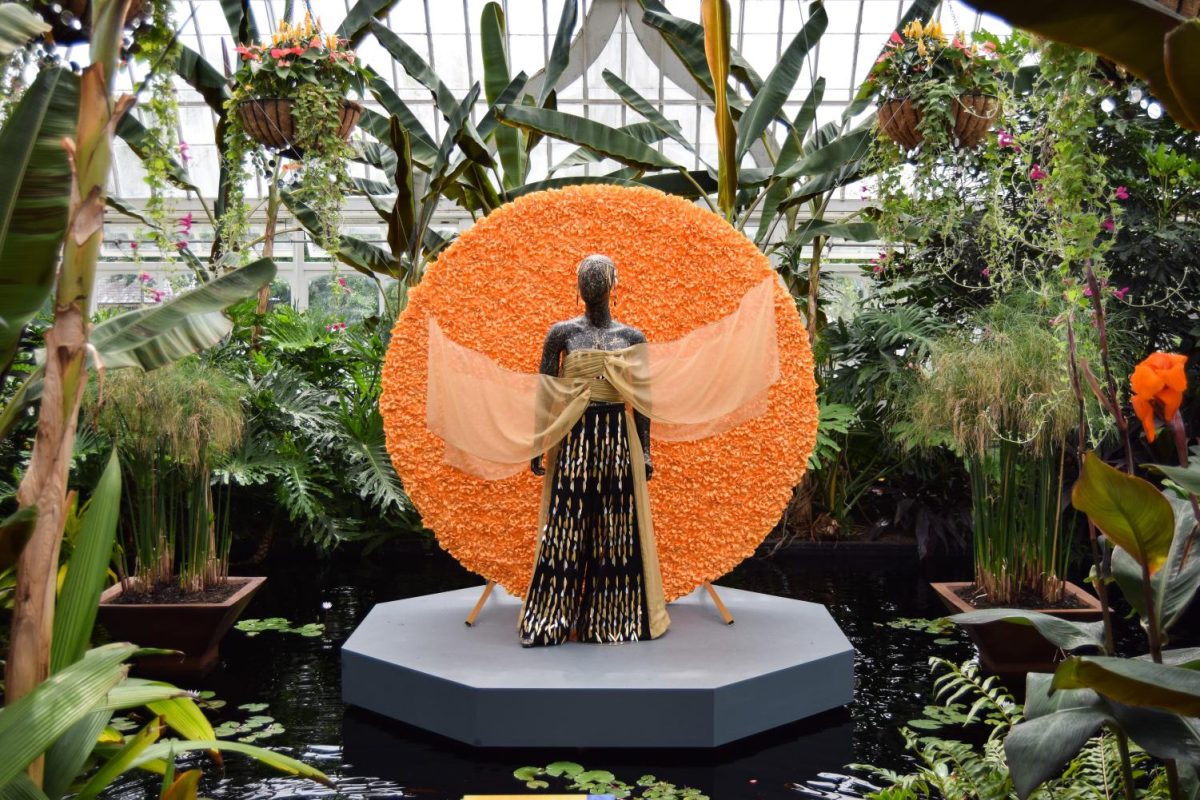 A gold costume hovers above a pond of blue water in the Victoria Room of the Phipps Conservatory. 