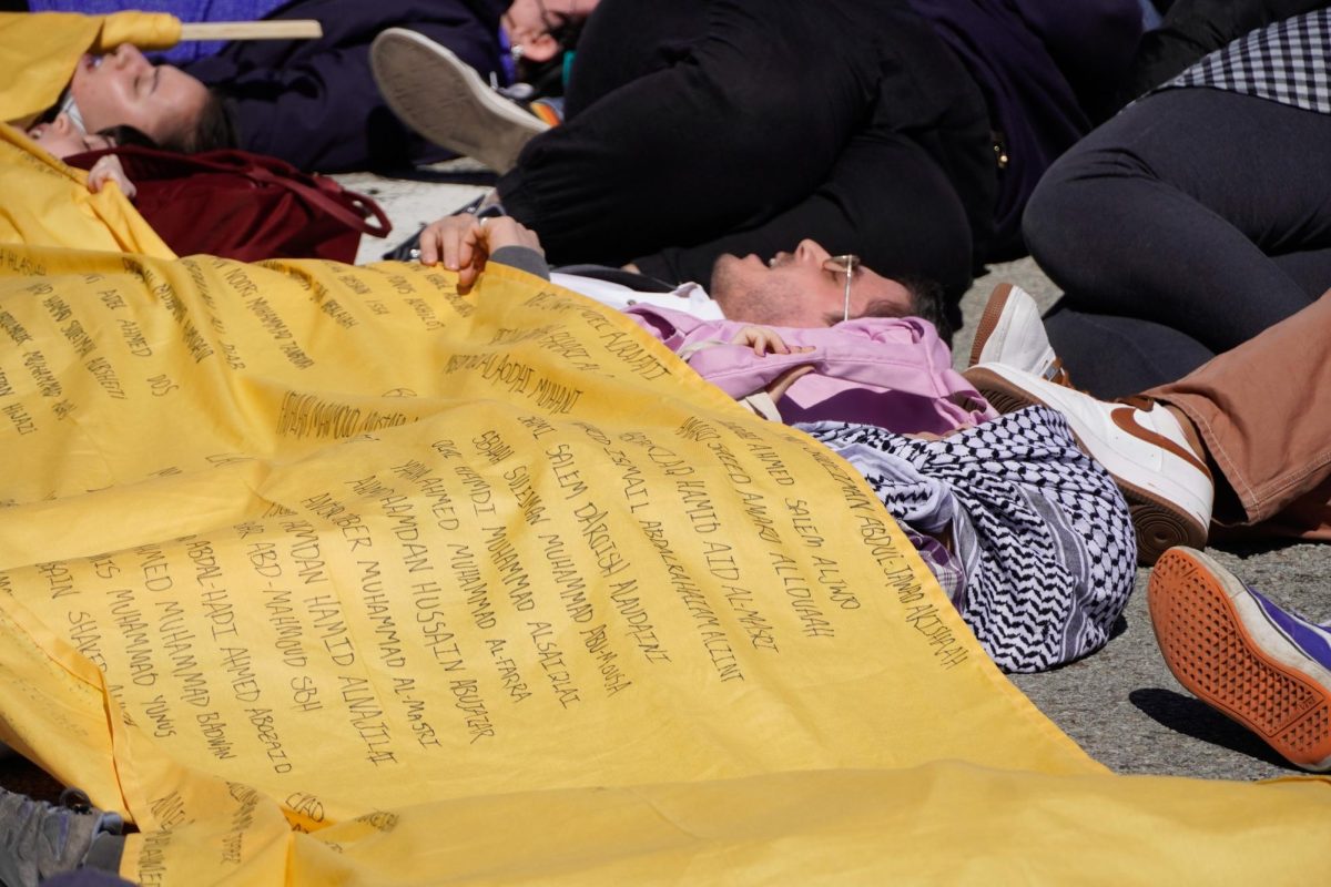 Protesters participate in a die-in while draped in a sign covered in names in front of the Cathedral of Learning on Friday. (Evan Fuccio | Staff Photographer)
