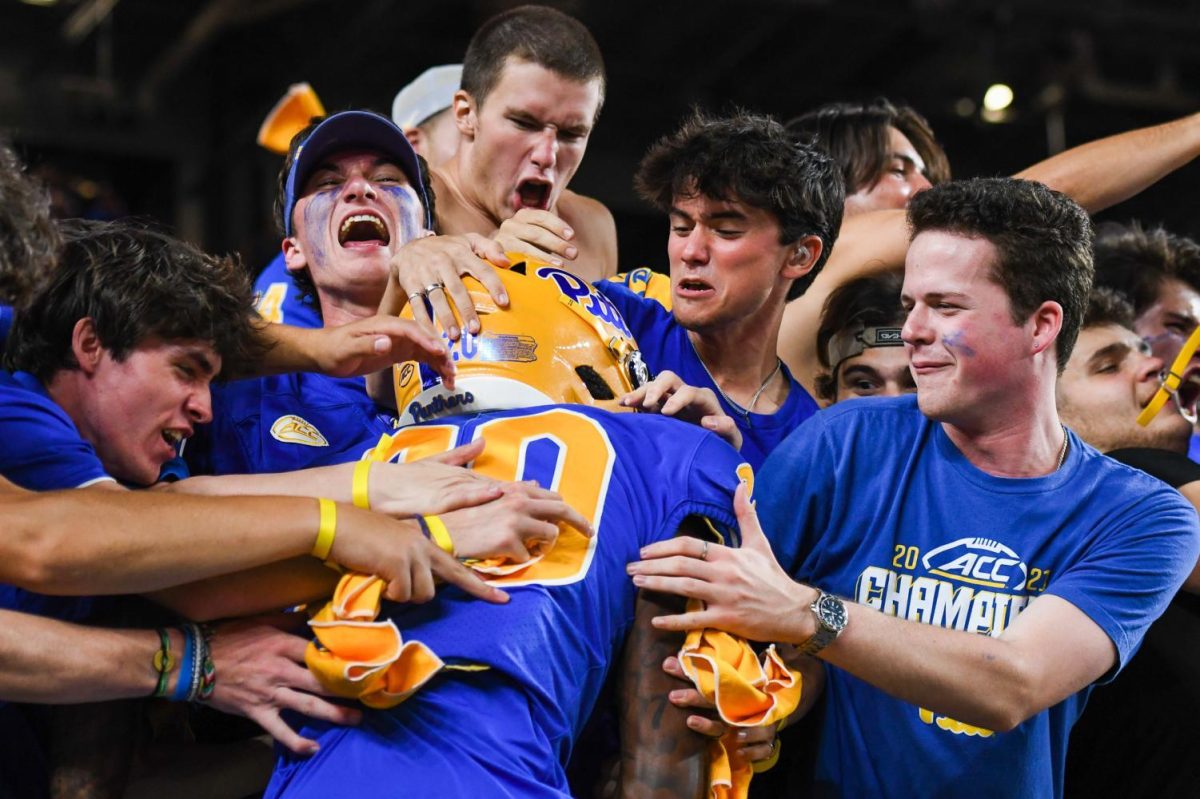 Students yell and grab first-year wide receiver Myles Alston (20) as they celebrate Pitt football's win over West Virginia on Sept. 1, 2022.