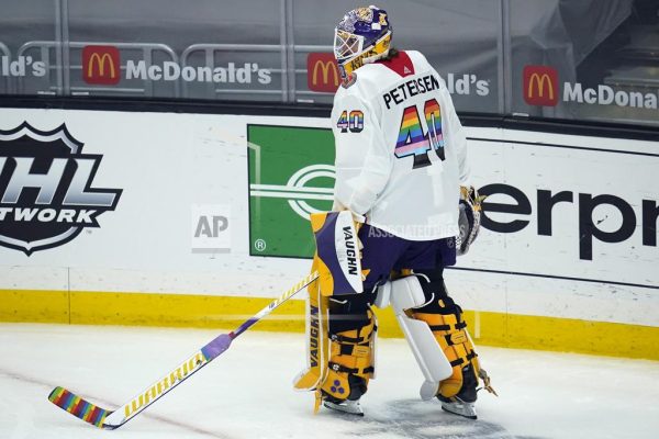 Los Angeles Kings goaltender Calvin Petersen (40) wears a Pride-themed jersey and holds a stick wrapped in rainbow tape for Pride Night while warming up before an NHL hockey game.

