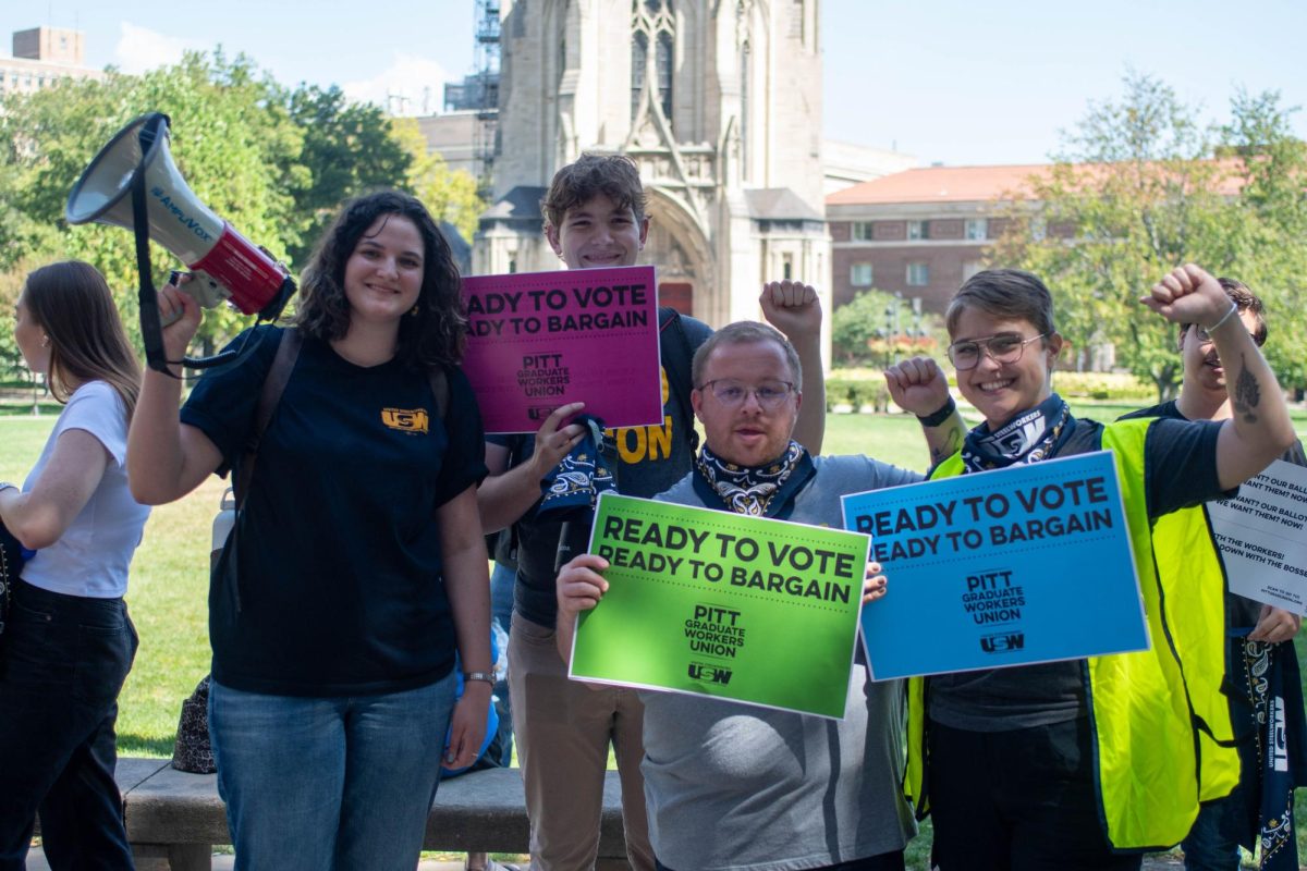 Rallygoers pose for a photo holding signs in support of the Pitt Grad Union on Tuesday outside of the Cathedral of Learning.