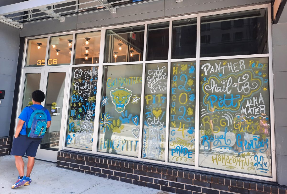 A student observes the festively decorated windows of HERE Pittsburgh apartments for Homecoming.
