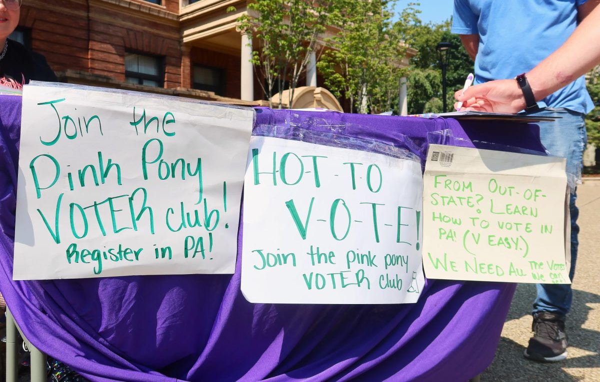 A voter registration table with signs encouraging people to register to vote.