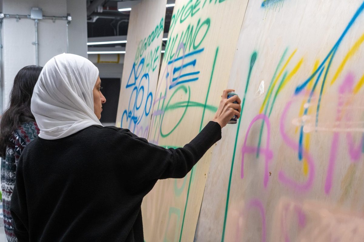 A student uses spray paint on a large piece of plywood.