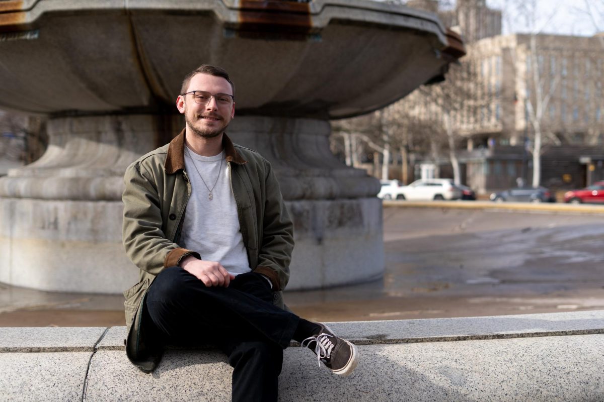 Graduate information sciences student James Sanchioli sits on a fountain in front of the Frick Fine Arts Building.
