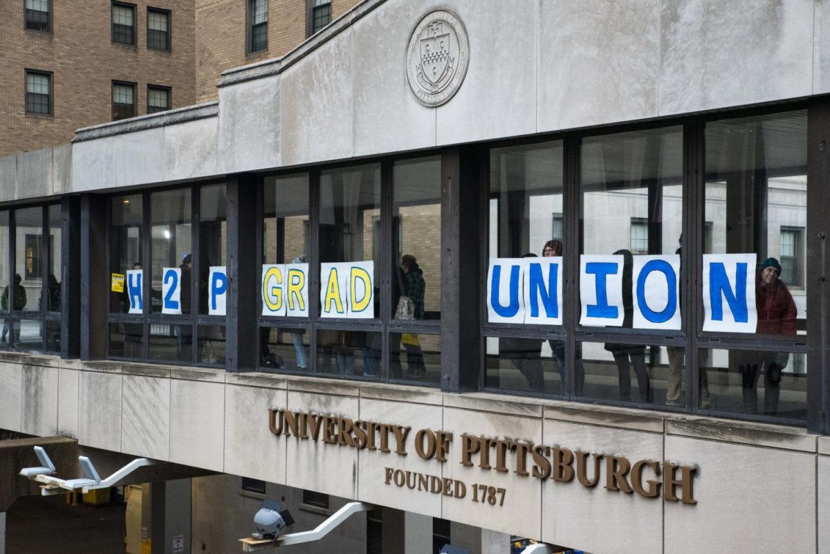 Grad union organizers hold signs against the windows of the Forbes Avenue sky bridge on Nov. 27, 2019.