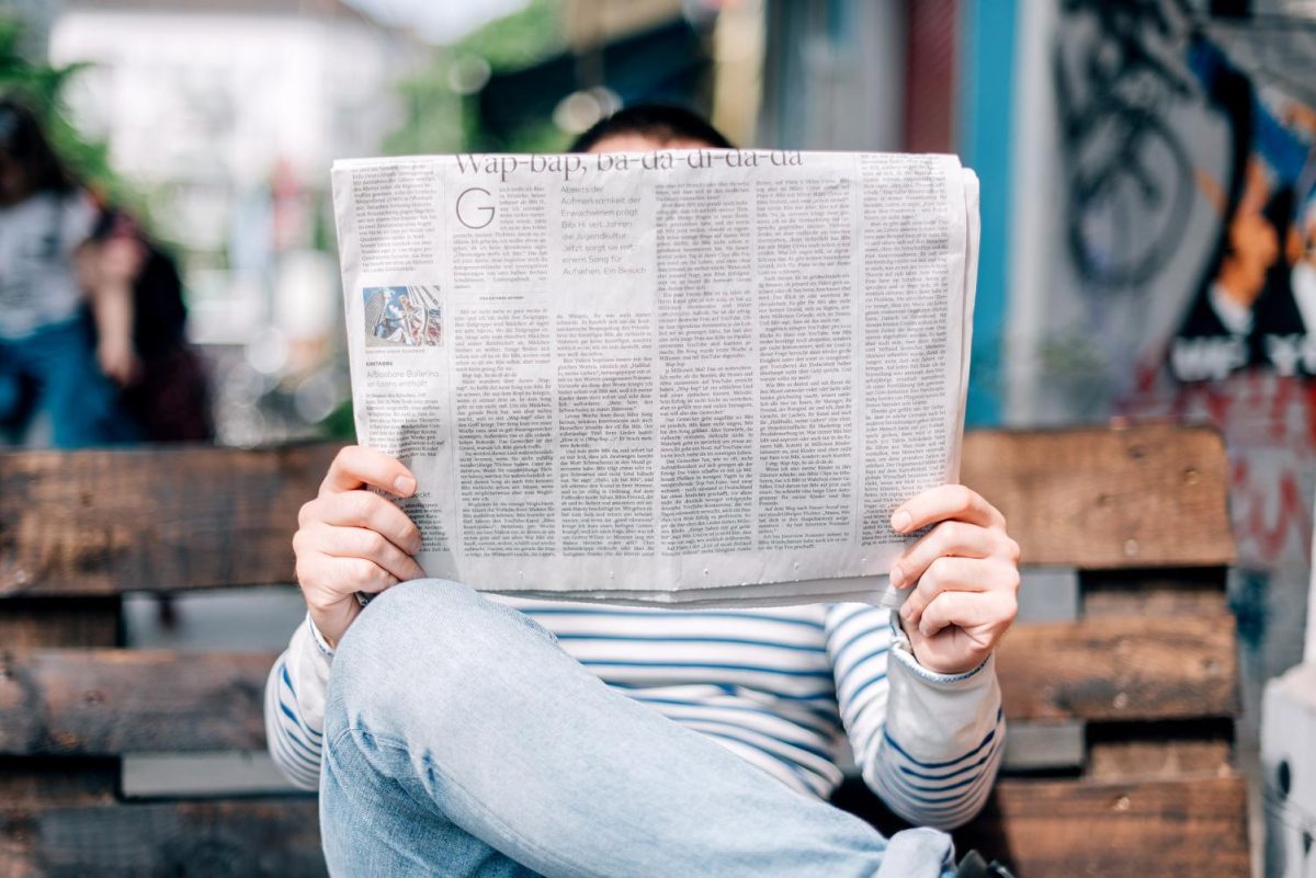 A person on a bench reads a newspaper.